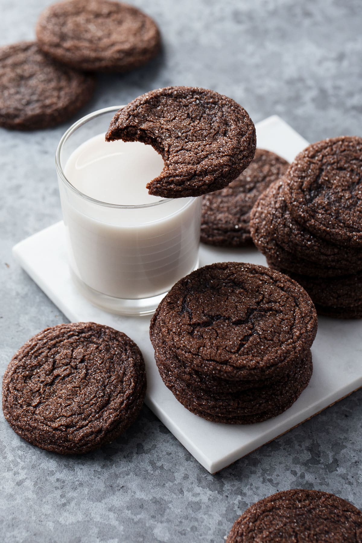 Chewy Chocolate Molasses Cookie with a bite taken out of it resting on top of a glass of milk, more cookies arranged around it.