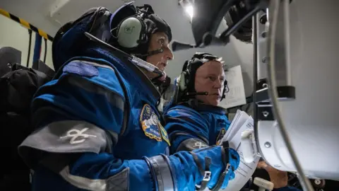 Nasa Both astronauts are in theri blue Boeing astronaut suits seated in the cockpit of the Starliner Capsule. 