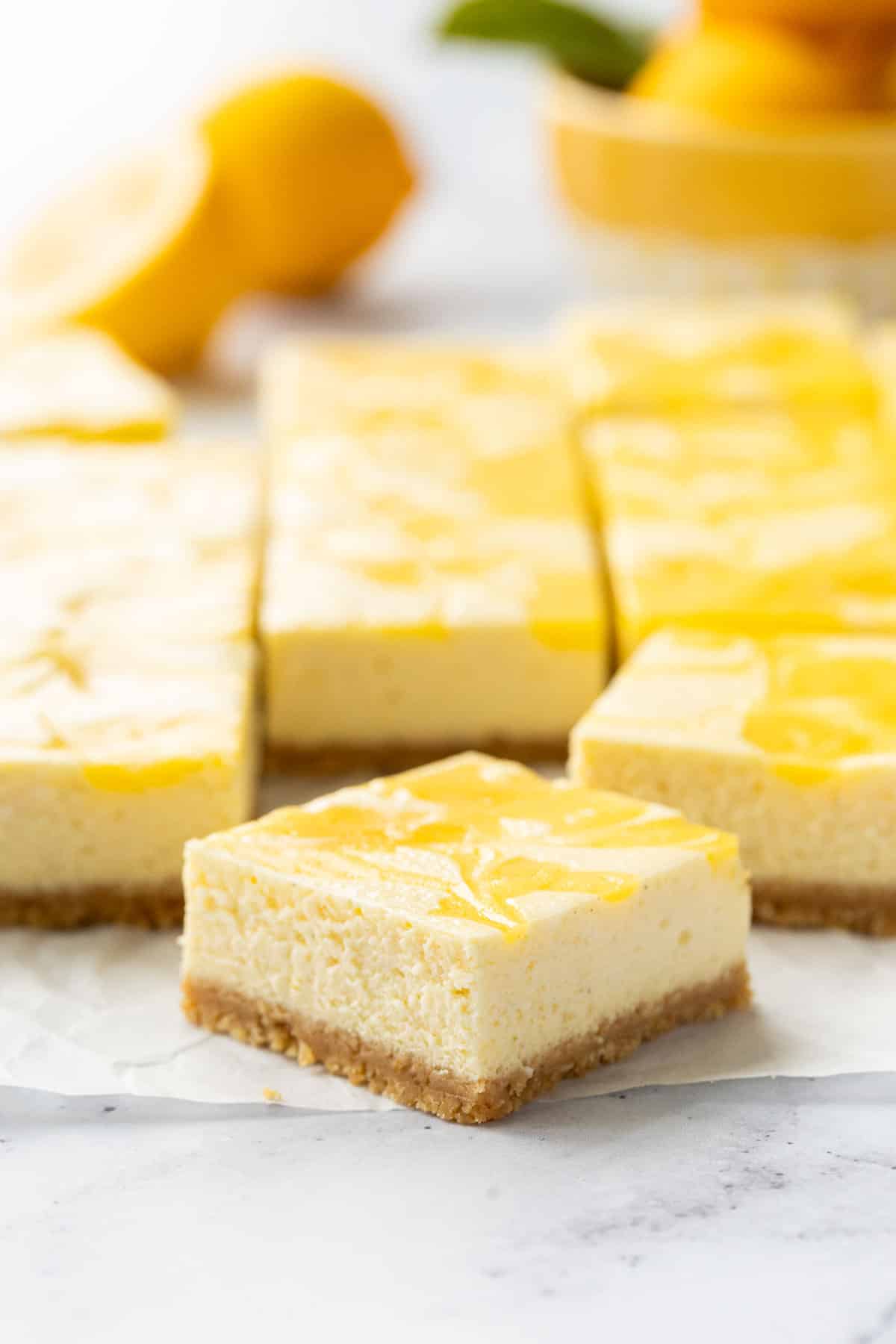 Closeup, perfectly cut square of lemon cheesecake bars, showing the cookie crust, cheesecake, and lemon curd swirl layers.