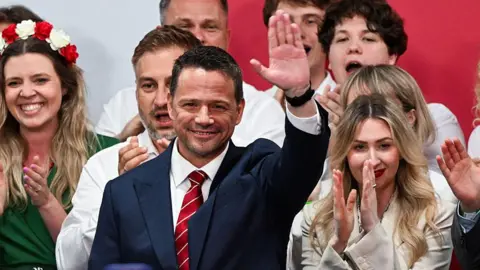 Getty Images Presidential candidate Rafal Trzaskowski raises his hand to greet supporters as his wife, Malgorzata, standing next to him, claps.