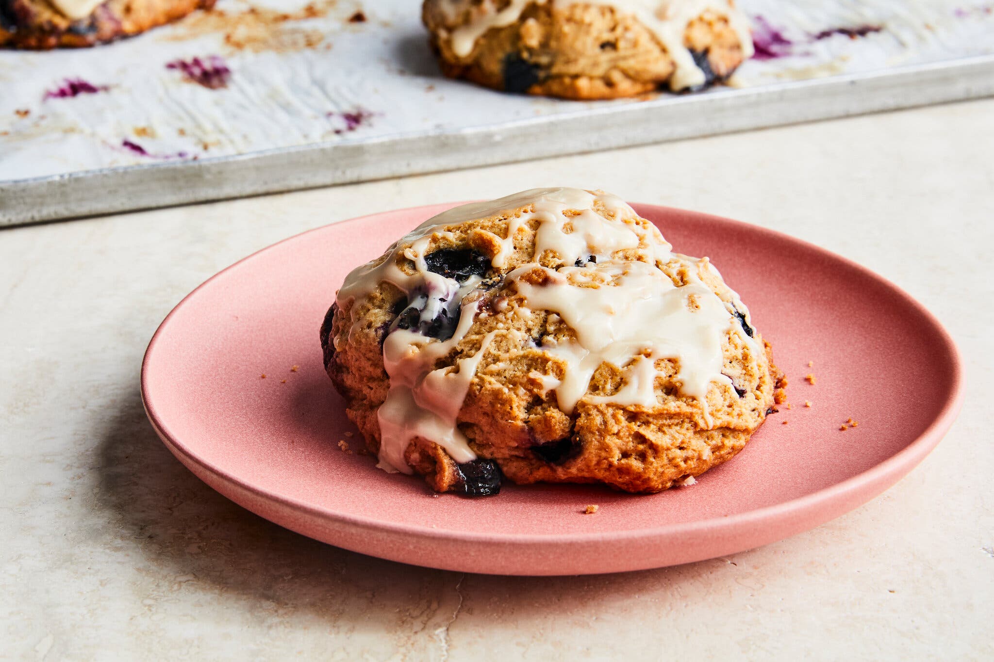 A side image of an icing-topped scone sitting on a pink plate.