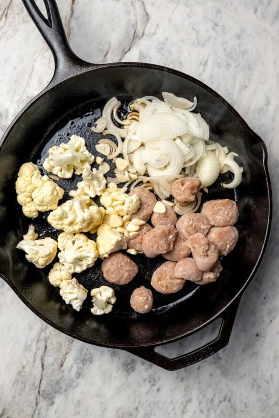 Sausage, cauliflower, and onions added to cast iron skillet.