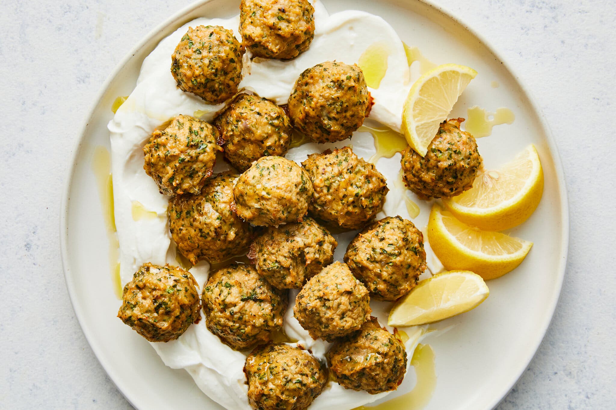 An overhead image of small chicken meatballs on a bed of yogurt next to lemon wedges.