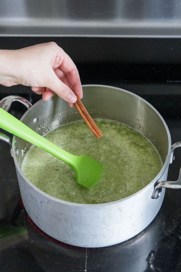 Adding a whole cinnamon stick to saucepan with jam mixture.