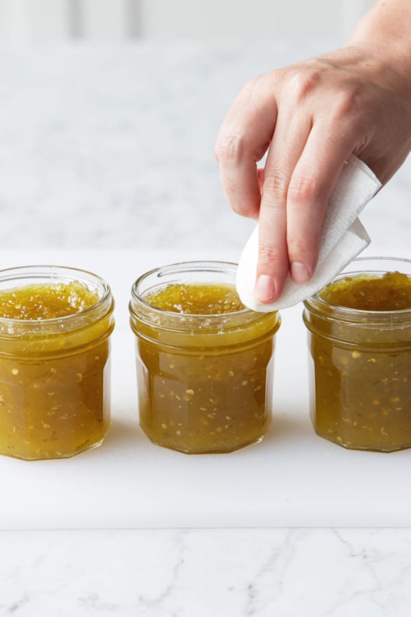 Wiping the rims of the canning jars to ensure the lids seal cleanly.