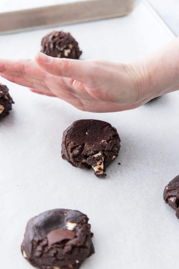 Pressing cookie dough balls into a puck shape using the ball of your hand.