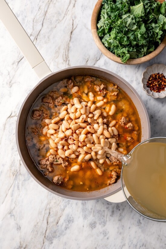 Pouring chicken stock into pot of white bean soup.