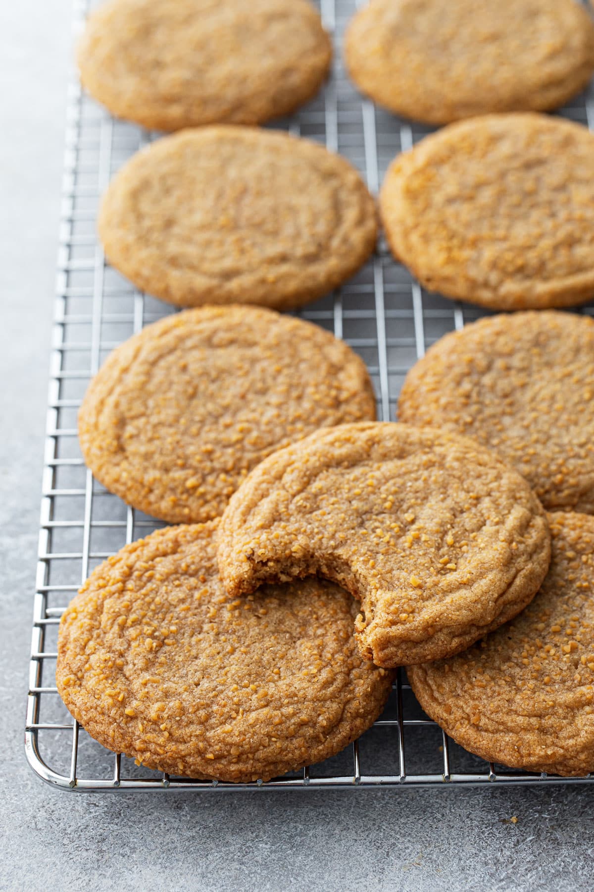 Chewy Maple Brown Butter Sugar Cookies on a wire cooling rack, one cookie on top with a bite taken out of it.