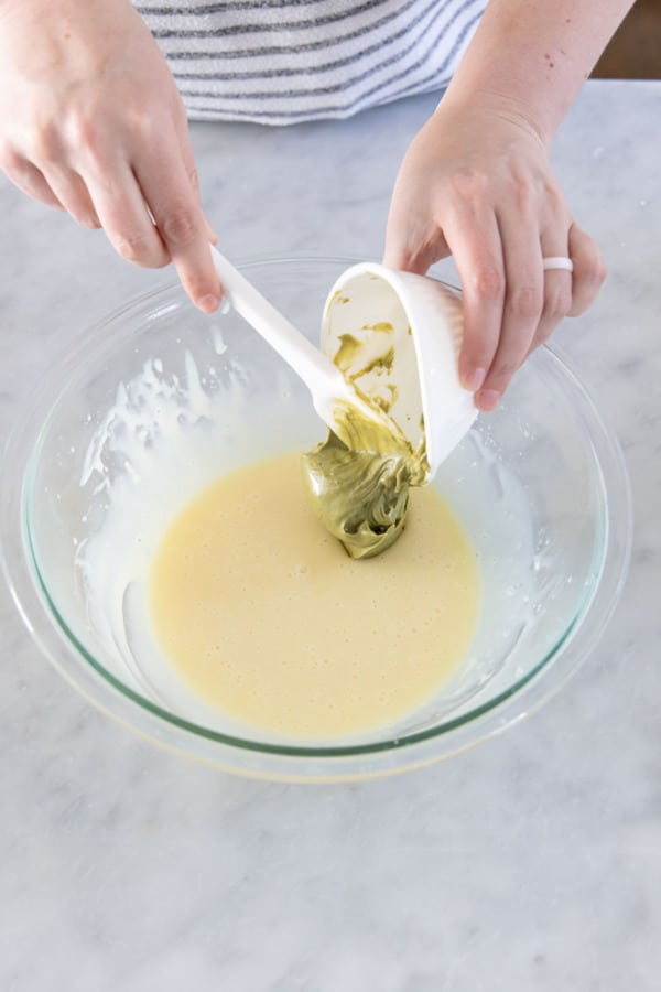 Adding pistachio cream paste to bowl with melted white chocolate and cream.