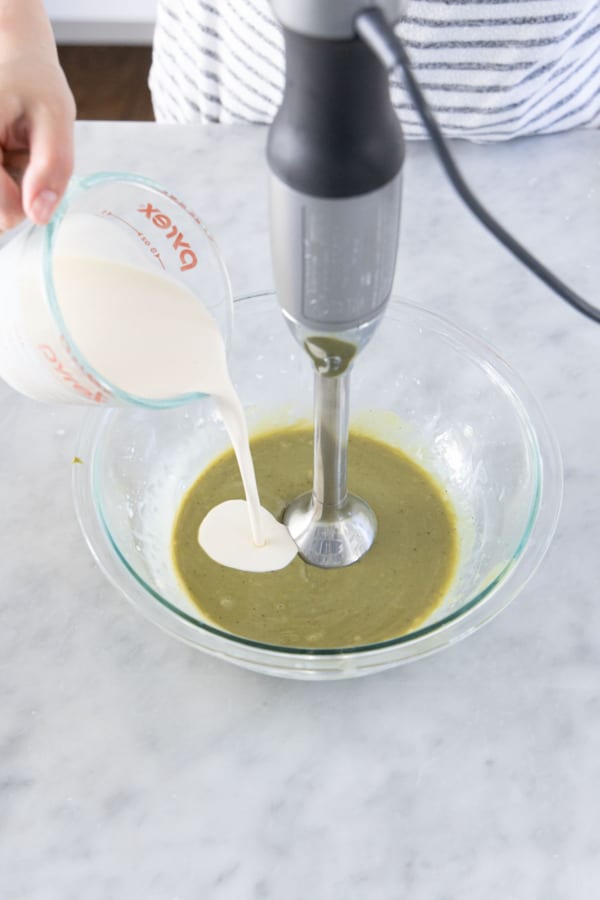 Immersion blender mixing pistachio ganache, while pouring in more heavy cream.