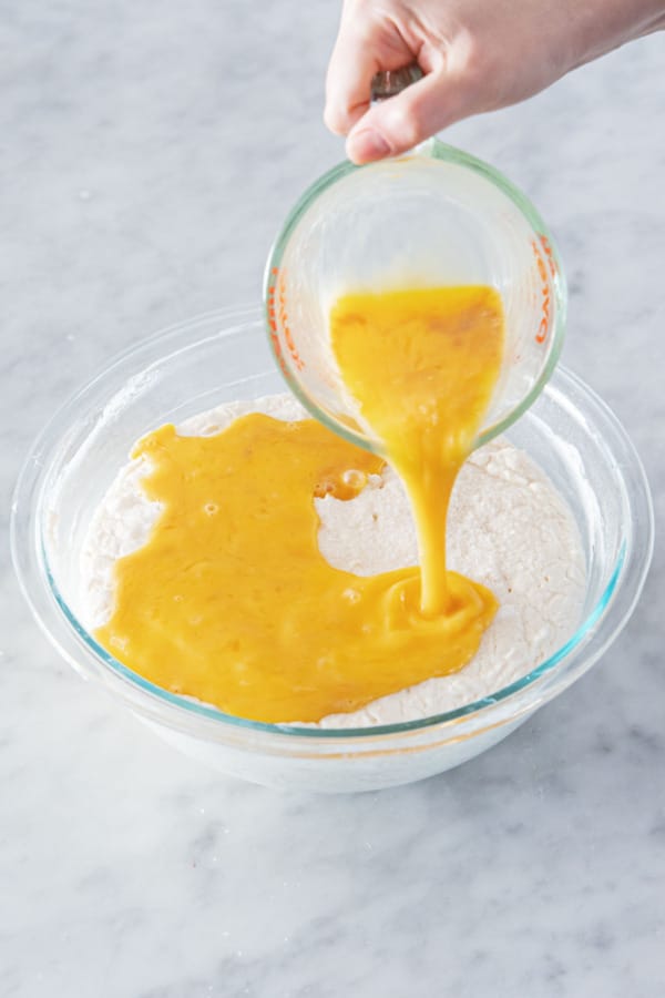 Adding lightly beaten eggs (beaten with vanilla) into mixing bowl with sourdough batter.